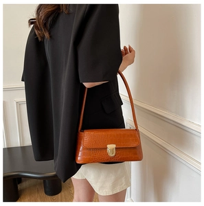 Brown crocodile embossed baguette bag with gold metal buckle worn by a model in a city look