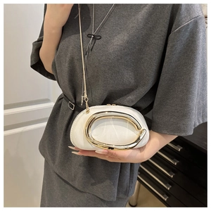 Detail of a chic cream mini box bag with a bold gold C-shaped metal handle and chain