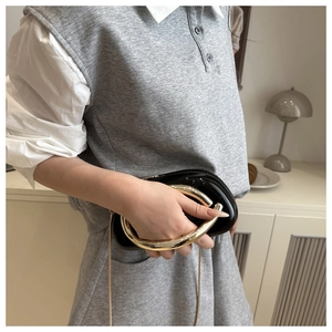 Détail du sac à main noir brillant avec poignée ronde dorée et chaîne métallique