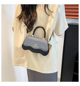 Detail of crossbody bag with wave-shaped bottom design and bicolor textured panels