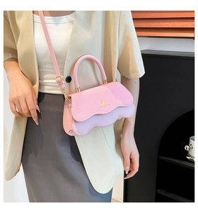 Detail of light pink shoulder bag with wavy flap design and gold hardware on a model