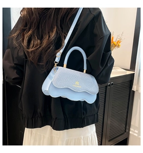 Detail of light blue crossbody bag featuring a wavy flap design and gold hardware logo