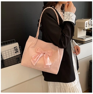 Close-up of pink suede tote bag featuring oversized bow and braided handle details
