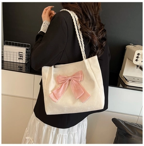 Detail of a creamy white tote bag featuring a large pink bow and woven rope shoulder strap