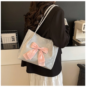 Detail of silver tote bag with pink satin bow and woven rope handles on a stylish model