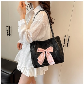 Close-up of black tote bag featuring a large pink bow and woven shoulder straps