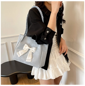 Detail of light blue suede tote bag featuring a large white bow and woven shoulder strap