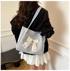 Detail of light blue tote bag featuring a large white bow and woven shoulder strap