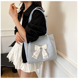 Detail of the woven shoulder strap and large white bow on a blue tote handbag