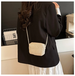Detailed back view of a cream woven crossbody bag shown against a black blazer and white skirt