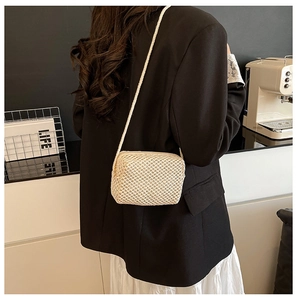 Detail of a beige hand-woven crossbody bag shown on a model with a black blazer
