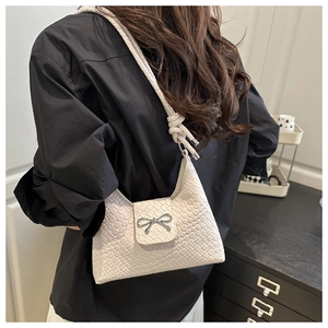 Model wearing a cream woven PU shoulder bag with a silver bow accent in a home setting