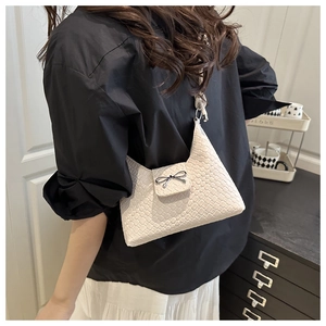 Détail du sac à bandoulière tressé crème avec boucle nœud noir et rabat magnétique