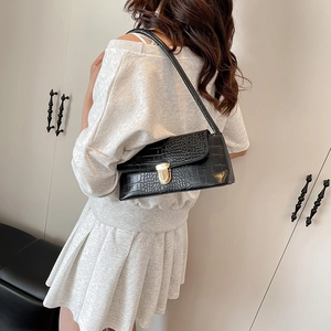 Elegant black crocodile pattern underarm bag with gold clasp shown on shoulder