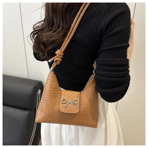 Détail d'un sac hobo tissé marron avec nœud en métal argenté et bandoulière à nœud décoratif