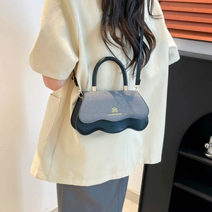 Denim and black leather crossbody bag with wavy base and gold metal handle on model