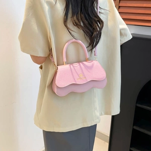 Pink trendy crossbody bag with wave bottom and gold logo carried by a model