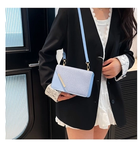 Close-up of light blue crossbody bag with gold diagonal metal trim and chain strap