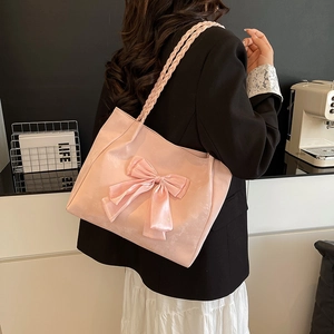 Pink tote bag with large satin bow and woven straps shown in a stylish lifestyle scene
