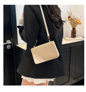 Détail d'un sac bandoulière bicolore avec boucle dorée sur une tenue de blazer noir