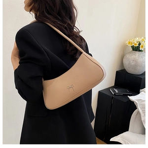 Close-up of a cream bow shoulder bag on a model wearing a black blazer in a studio
