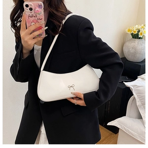 Detail of white half-moon baguette bag with a sleek metallic bow and leather shoulder strap