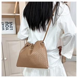 Détail d'un sac seau tressé marron avec une plaque métallique dorée distinctive