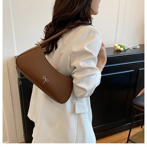 Schicke dunkelbraune Leder-Umhängetasche mit silberner Schleife zu weißem Blazer