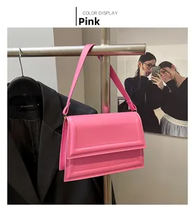 Detalle de un bolso bandolera de cuero rosa con costuras geométricas en un soporte de tienda