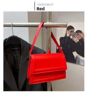 Detalle de un bolso bandolera rectangular rojo brillante colgado junto a un traje negro