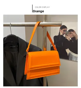 Detalle de un bolso de hombro rectangular naranja con costuras finas en una percha de metal
