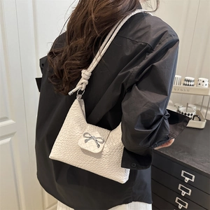 White woven shoulder bag with silver bow accent and knotted strap shown on model