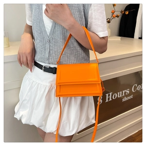 Bolso bandolera de cuero naranja brillante combinado con una falda plisada blanca de moda