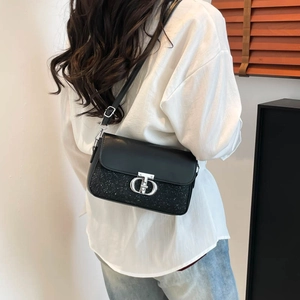 Sac à bandoulière noir tendance avec fermoir métallique CD argenté porté à l'épaule du mannequin