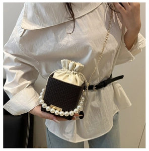 Detail view of brown bucket bag with pearl handle and golden chain on a model