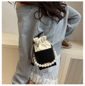 Model wearing a mini black bucket bag with pearl handle and metal chain strap details