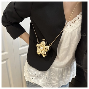 Close-up of golden flower mini evening bag with pearl center worn with a black blazer
