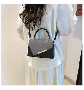Rear view of model wearing black crossbody bag with gold metal bar and textured fabric