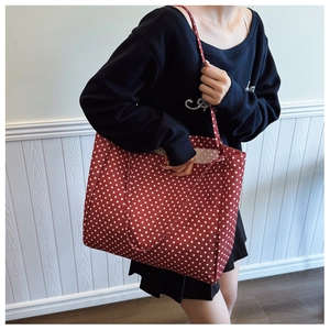 Detail of red canvas tote bag with white polka dots featuring reinforced double handles