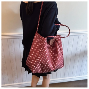 Detail of red polka dot canvas tote bag with dual straps worn by a model in interior