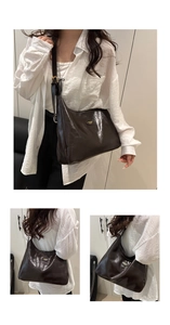 Detail of dark brown glossy patent leather shoulder bag with golden logo and fine texture