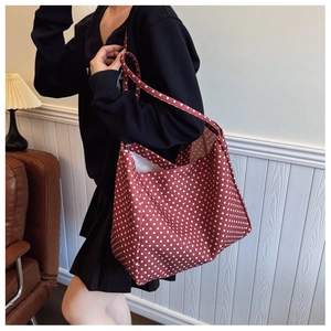 Detailed view of red canvas tote bag with white polka dots carried on shoulder