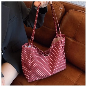 Detail of red and white polka dot canvas tote bag held by model on leather sofa