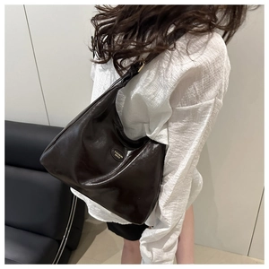 Detailed close-up of dark brown glossy leather hobo bag with oval metal fashion emblem