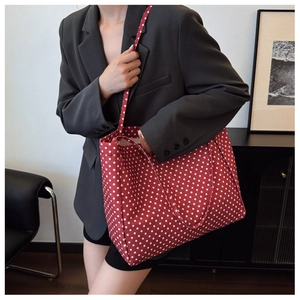 Detail of red canvas tote bag with white polka dots worn by a model in a modern room