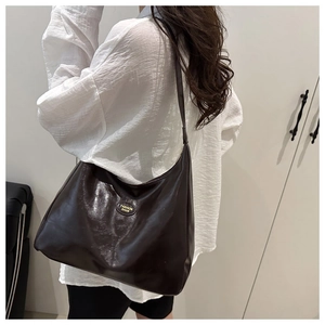 Detail of dark brown tote bag with metal logo tag shown from back side angle