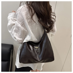 Close-up of a dark brown crescent tote bag featuring a gold metal brand plate on the side