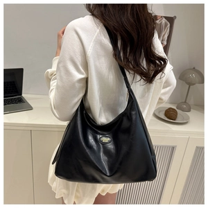 Detail of black leather hobo bag with gold fashion logo on minimalist desk setting