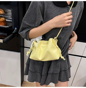 Detail of soft yellow pleated bucket bag with decorative pearls and lace bow detail