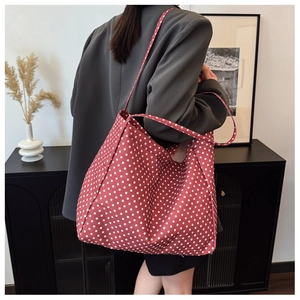 Detail view of large red canvas tote bag with white polka dots worn by model